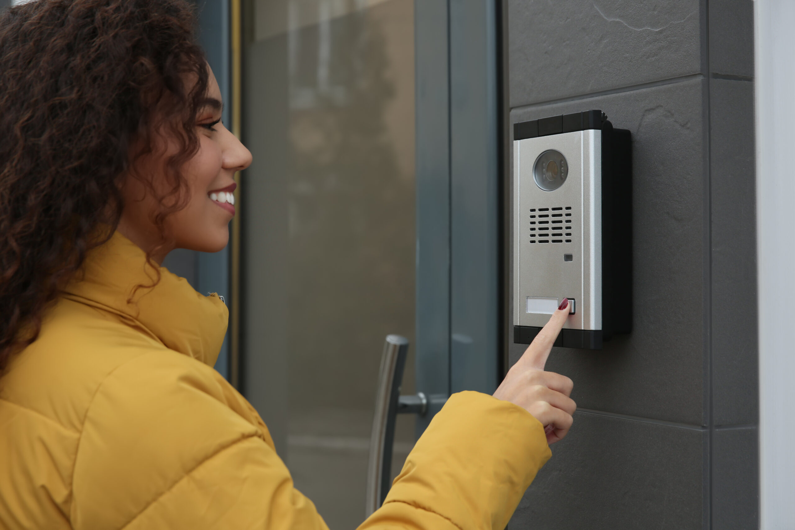 Young African-American woman ringing intercom with camera near b